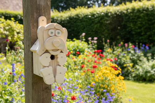 Wooden dog character bird box mounted on a post in a sunny cottage garden with flowers